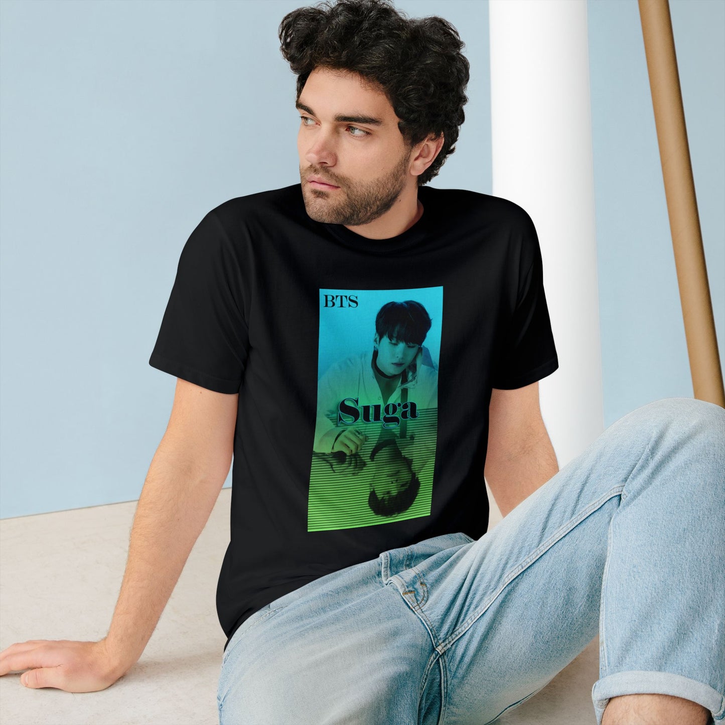 Man wearing a unisex combed organic cotton T-shirt in black, featuring Agust D (Suga of BTS) in a turquoise-to-green gradient design. His clear image sits above, while a mirrored reflection below is overlaid with horizontal scan lines, suggesting a digital echo or filtered version of the original. From ModeK Vetements.
