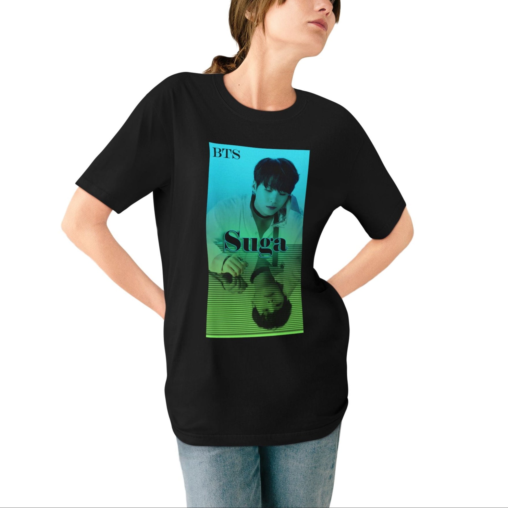 Woman wearing a unisex combed organic cotton T-shirt in black, featuring Agust D (Suga of BTS) in a turquoise-to-green gradient design. His clear image sits above, while a mirrored reflection below is overlaid with horizontal scan lines, suggesting a digital echo or filtered version of the original. From ModeK Vetements.