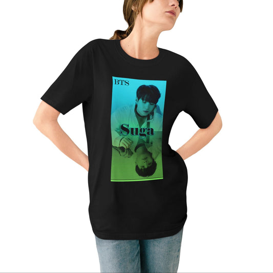 Woman wearing a unisex combed organic cotton T-shirt in black, featuring Agust D (Suga of BTS) in a turquoise-to-green gradient design. His clear image sits above, while a mirrored reflection below is overlaid with horizontal scan lines, suggesting a digital echo or filtered version of the original. From ModeK Vetements.