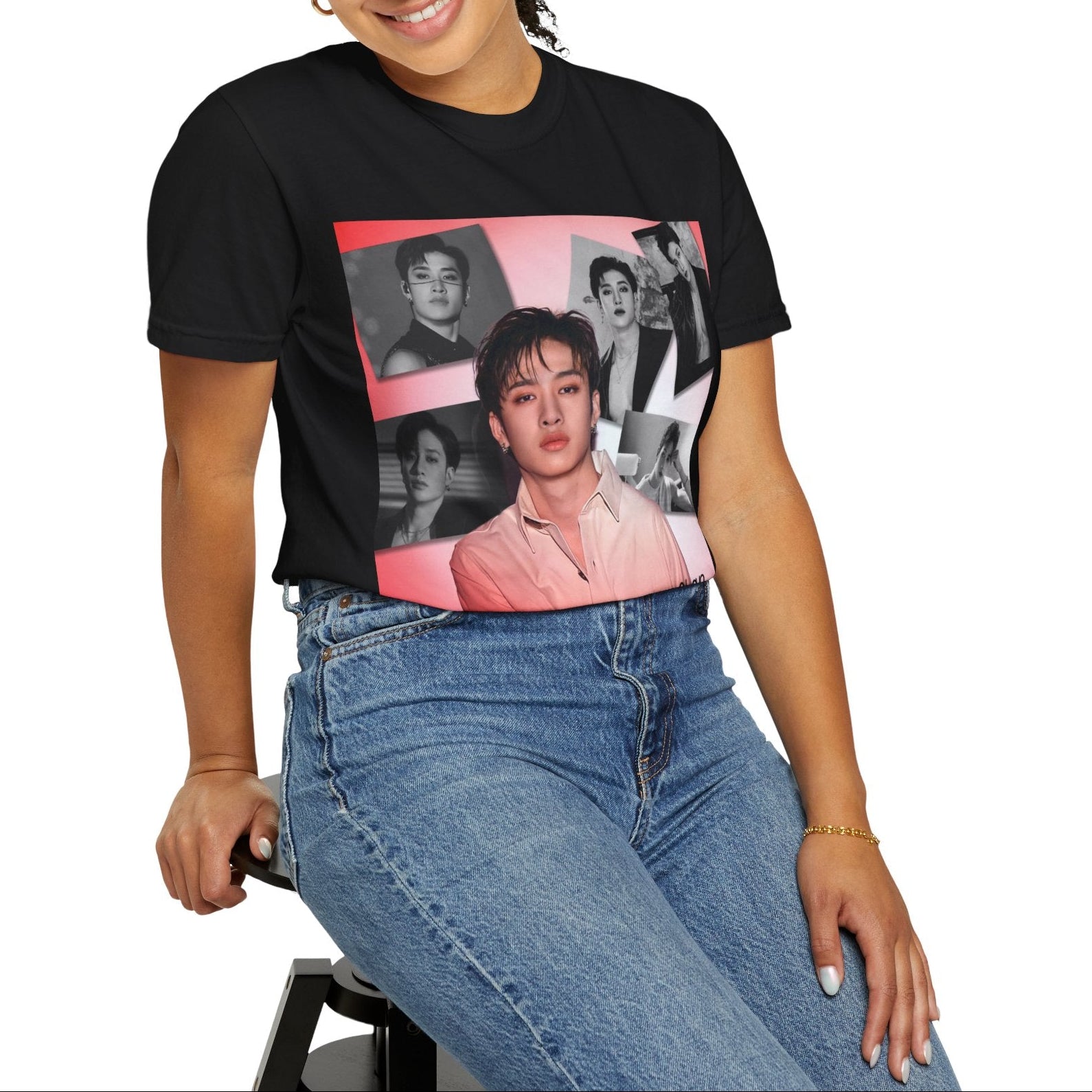 Model sitting on a stool and showcasing the Bang Chan Stray Kids Unisex T-Shirt in black, featuring a soft pink glow and black-and-white portraits. A design capturing his warmth, quiet confidence, and magnetic presence. 100% ring-spun cotton from ModeK Vetements.