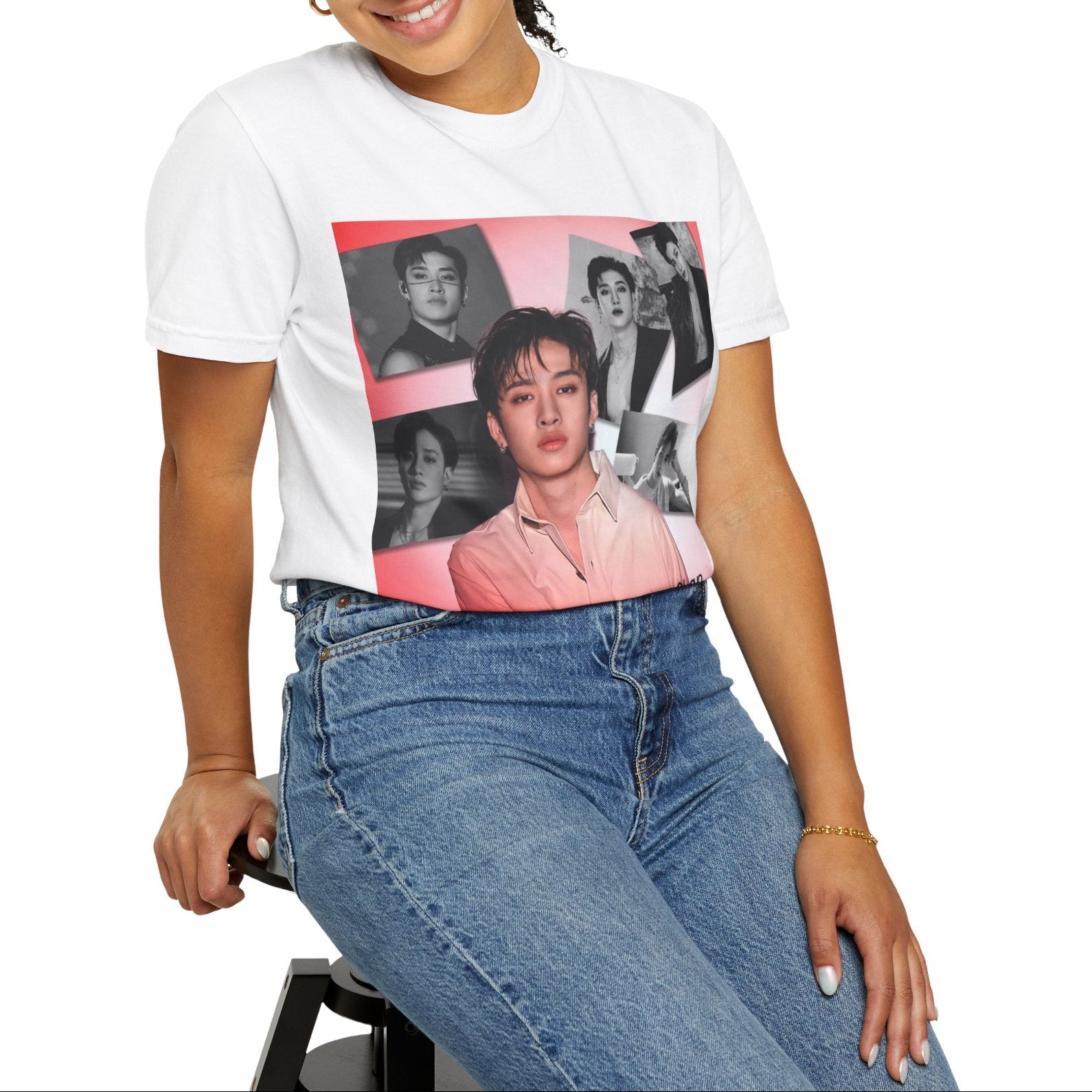 Model sitting on a stool and showcasing the Bang Chan Stray Kids Unisex T-Shirt in white, featuring a soft pink glow and black-and-white portraits. A design capturing his warmth, quiet confidence, and magnetic presence. 100% ring-spun cotton from ModeK Vetements.