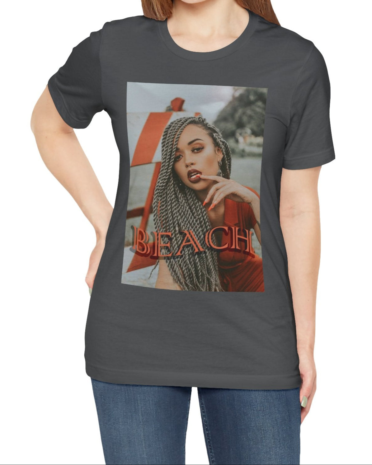 Portrait of a confident woman with long braids posing in front of an orange-and-white no-entry sign, printed on a unisex T-shirt in asphalt, with the word “BEACH” in bold orange lettering. ModeK Vetements.