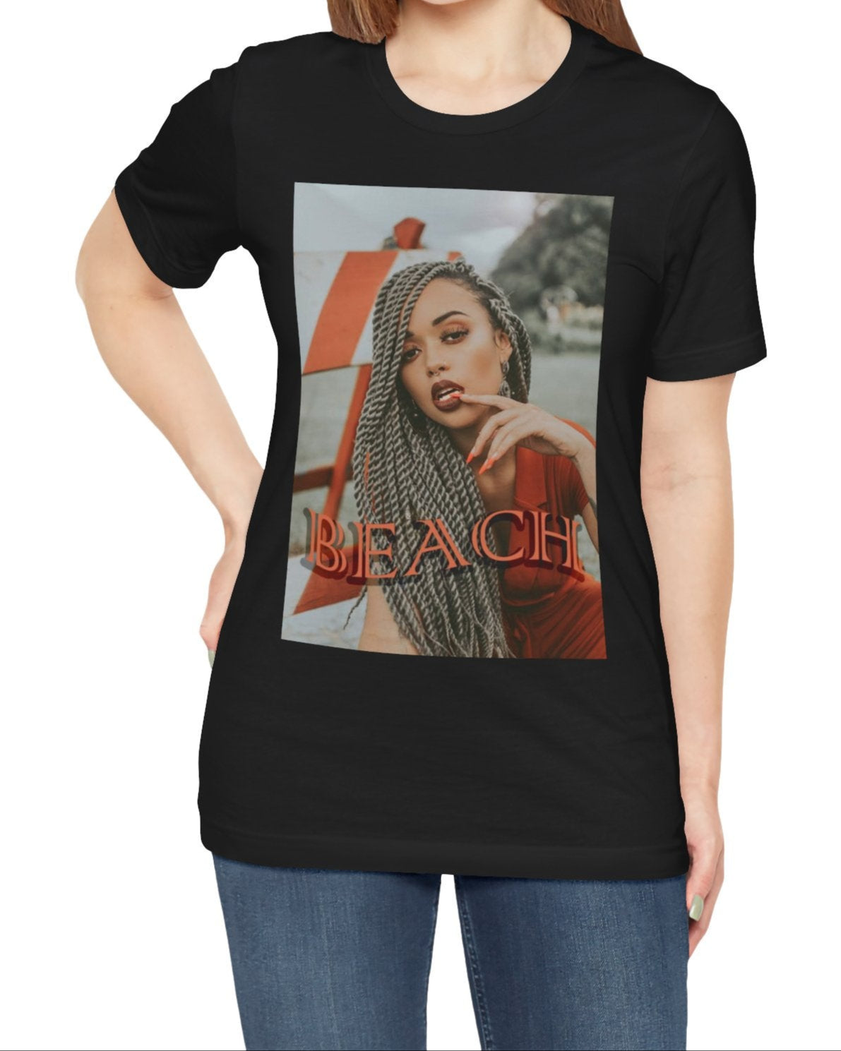 Portrait of a confident woman with long braids posing in front of an orange-and-white no-entry sign, printed on a unisex T-shirt in black, with the word “BEACH” in bold orange lettering. ModeK Vetements.