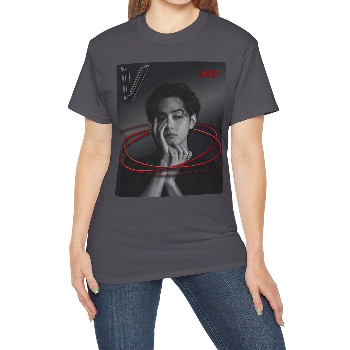 Model showcasing the unisex 100% cotton T-shirt in charcoal. The front of the shirt displays a high-contrast black-and-white portrait of K-pop star V (Kim Taehyung) looking forward with a contemplative expression. Encircling him are vibrant red, glowing 3D oval rings. A styled "V" appears in the top-left corner and a red "BTS" logo in the top-right corner. From ModeK Vetements.