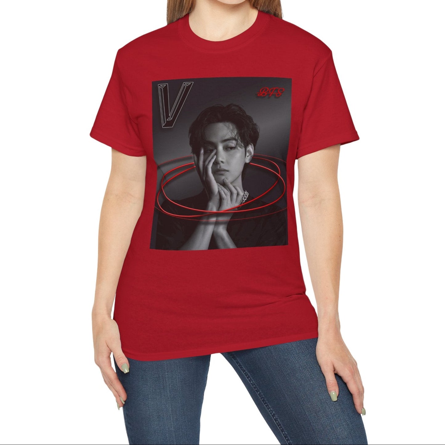Model showcasing the unisex 100% cotton T-shirt in cherry red. The front of the shirt displays a high-contrast black-and-white portrait of K-pop star V (Kim Taehyung) looking forward with a contemplative expression. Encircling him are vibrant red, glowing 3D oval rings. A styled "V" appears in the top-left corner and a red "BTS" logo in the top-right corner. From ModeK Vetements.
