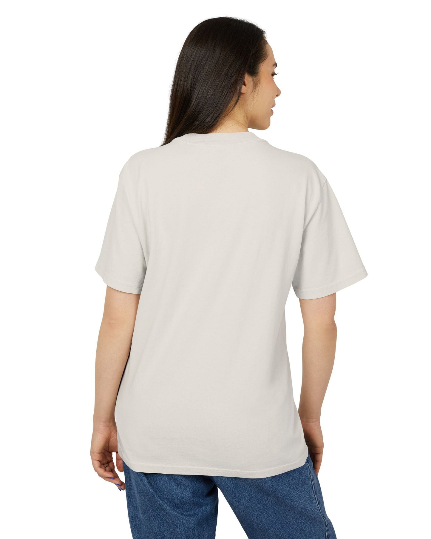 Back of the Unisex heavy carded cotton T-shirt in faded bone with a boxy fit, featuring a woman who sits in front of a softly lit vanity mirror, framed by diagonal tones of pine and sea green. Her expression is poised and calm, capturing quiet confidence without performance. From ModeK Vetements.