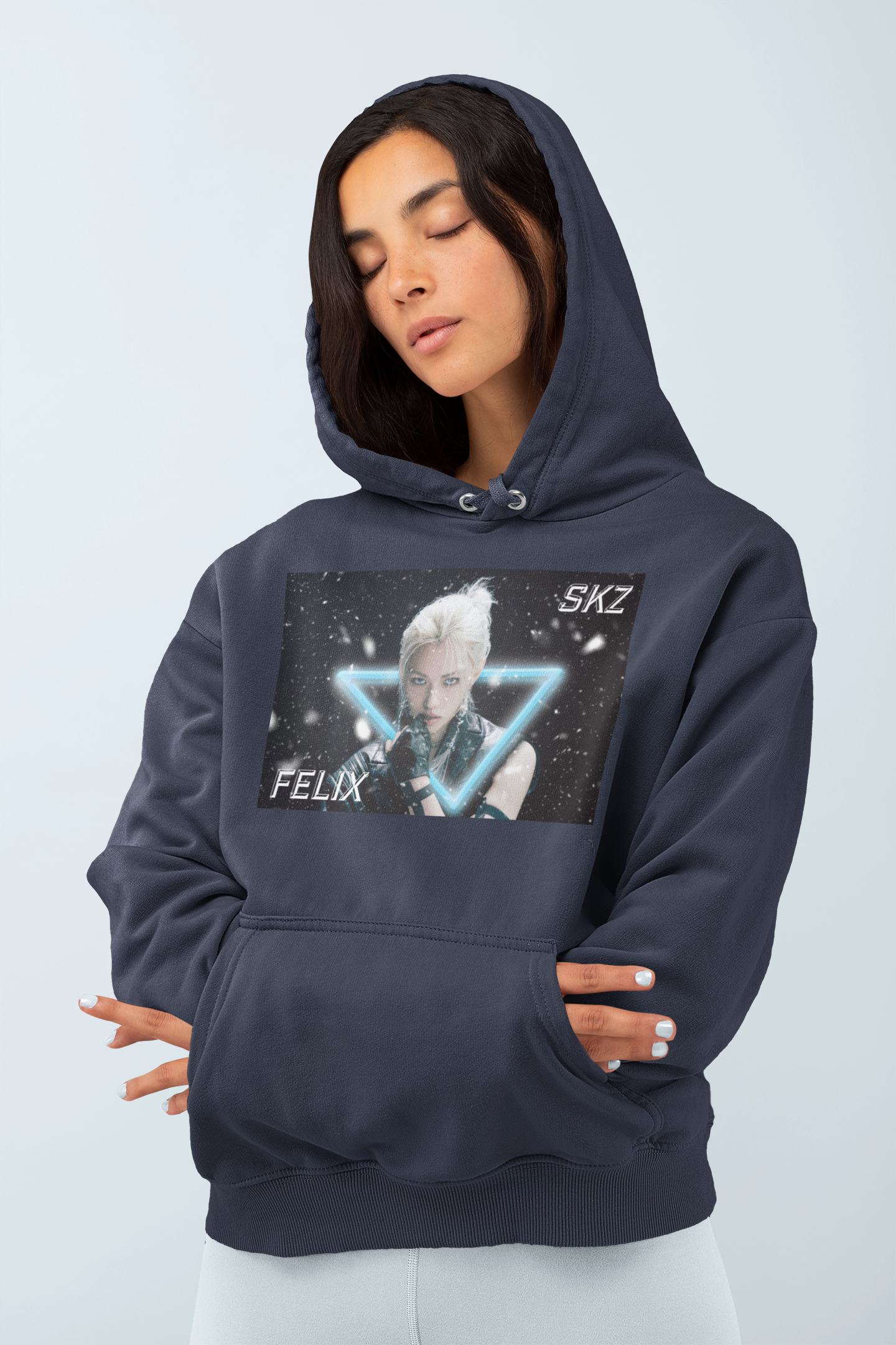 Model showcasing the Unisex cotton-poly blend hoodie in navy with closed eyes, featuring a visual print of Felix from Stray Kids, framed by a glowing blue neon triangle amid falling snow on a dark background. From ModeK Vetements.