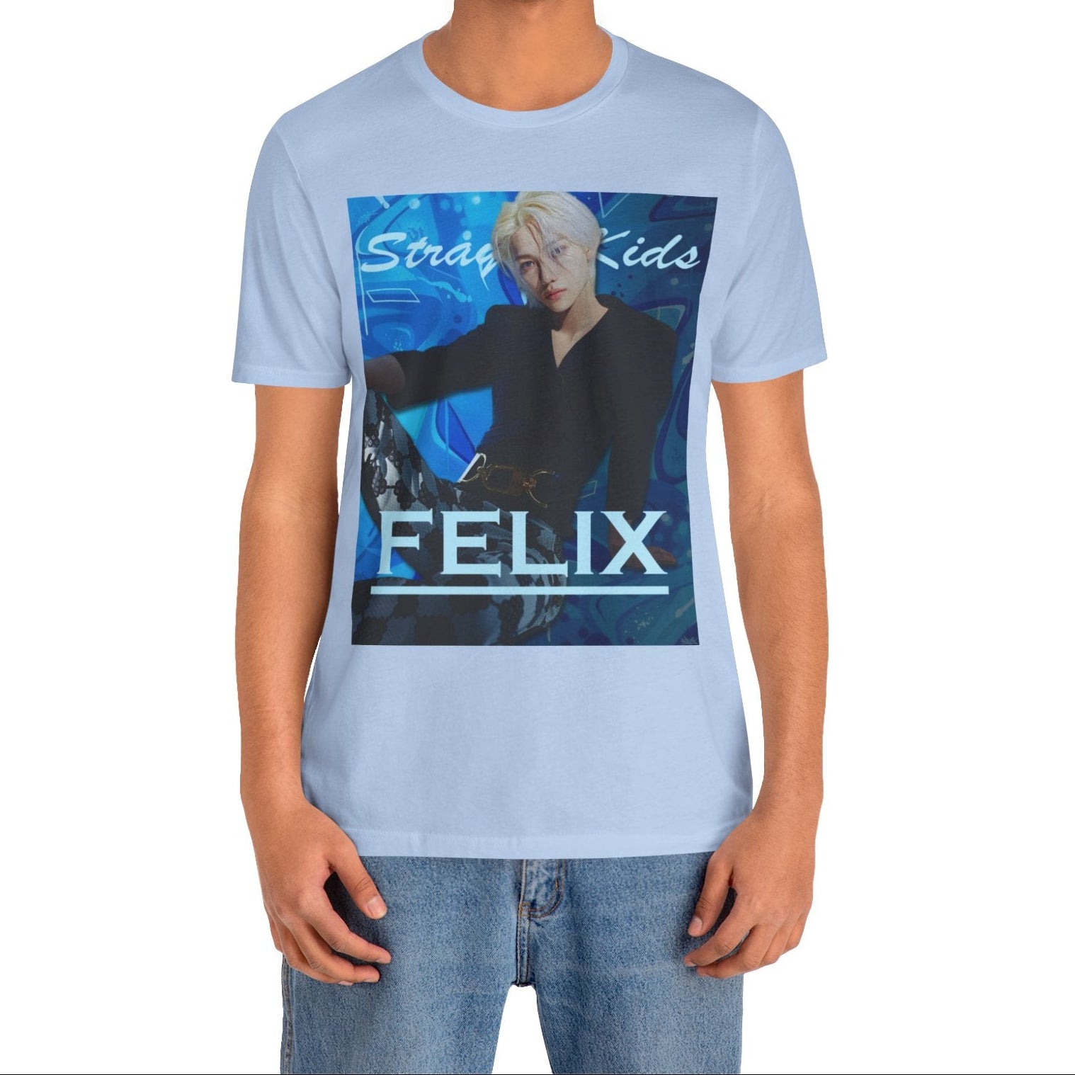 Male model showcasing the unisex, 100% airlume combed & ring-spun cotton t-shirt in baby blue, featuring a graphic design. It shows Felix from Stray Kids in a provocative pose, wearing a structured black suit jacket and oriental-style patterned pants. The background is a multi-toned blue graffiti. From ModeK Vetements.