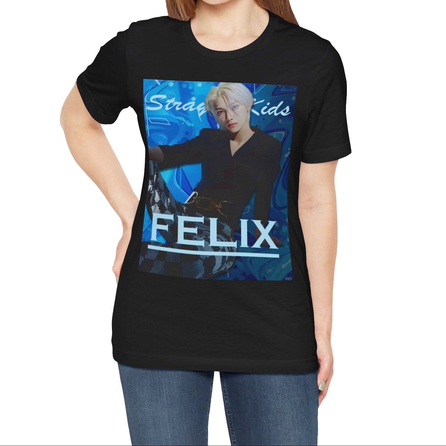Female model showcasing the unisex, 100% airlume combed & ring-spun cotton t-shirt in black, featuring a graphic design. It shows Felix from Stray Kids in a provocative pose, wearing a structured black suit jacket and oriental-style patterned pants. The background is a multi-toned blue graffiti. From ModeK Vetements.