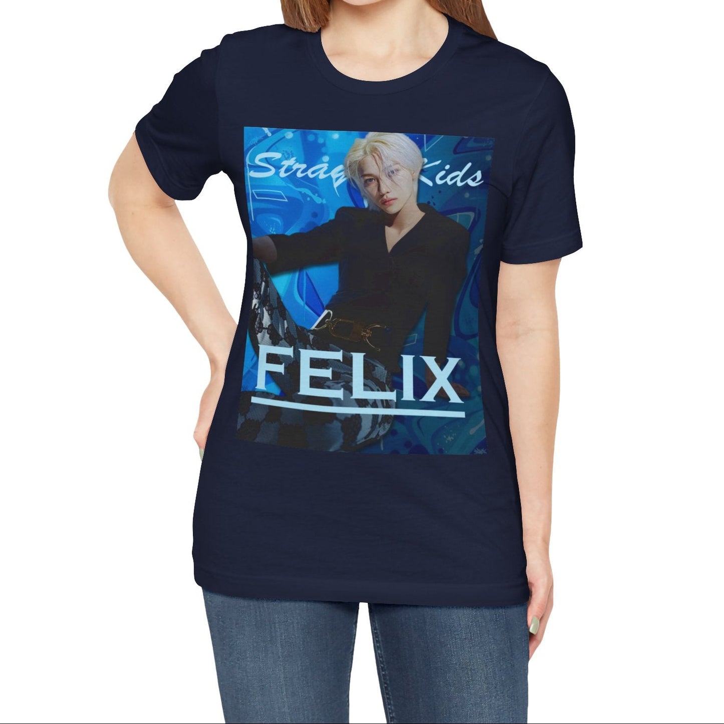 Female model showcasing the unisex, 100% airlume combed & ring-spun cotton t-shirt in navy, featuring a graphic design. It shows Felix from Stray Kids in a provocative pose, wearing a structured black suit jacket and oriental-style patterned pants. The background is a multi-toned blue graffiti. From ModeK Vetements.