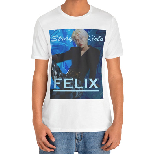 Male model showcasing the unisex, 100% airlume combed & ring-spun cotton t-shirt in white, featuring a graphic design. It shows Felix from Stray Kids in a provocative pose, wearing a structured black suit jacket and oriental-style patterned pants. The background is a multi-toned blue graffiti. From ModeK Vetements.