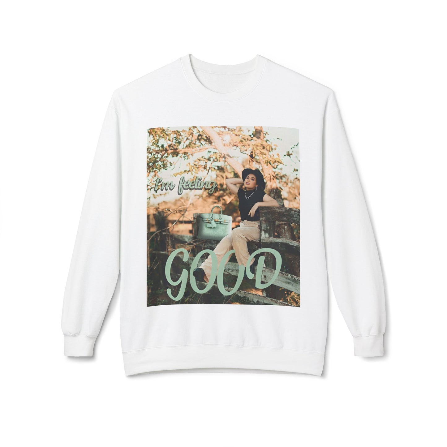 Hanging unisex sweatshirt in white featuring a photo of a woman in beige trousers and black top on a rustic fence. The gum leaf green “I’m feeling GOOD” text echoes the handbag and wraps visually around her legs. — From ModeK Vetements
