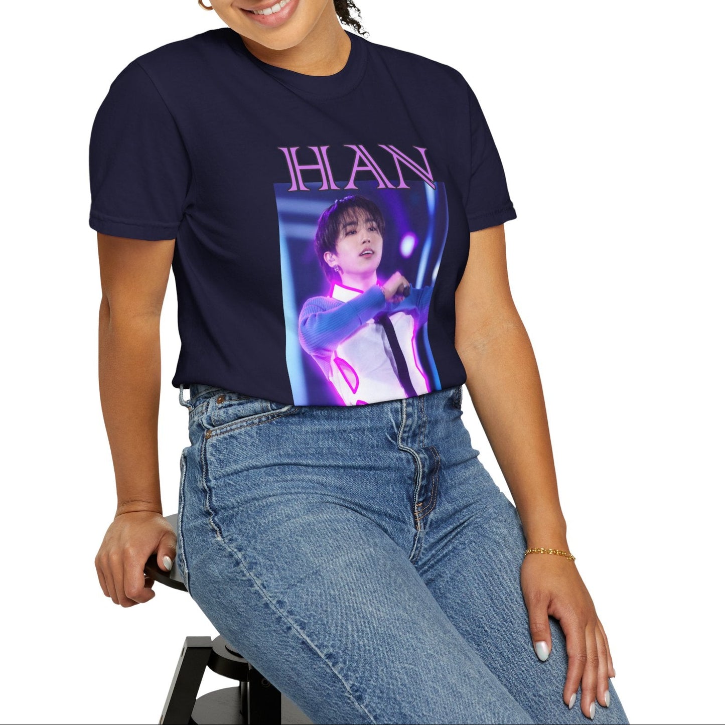 Model sitting on a stool and showcasing the Han Stray Kids Unisex T-Shirt in true navy – Neon Energy. A striking design featuring Han performing on stage, outlined in bold pink neon lights. The glowing effect adds a futuristic, high-energy feel, capturing his electrifying stage presence. 100% ring-spun cotton from ModeK Vetements.