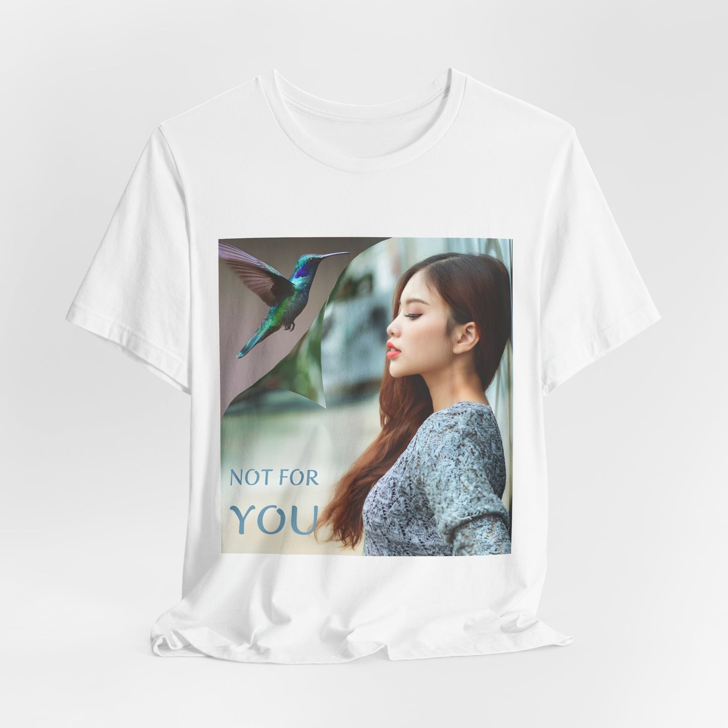 Draped Unisex airlume combed, ring-spun cotton T-shirt in white, featuring a turning-page effect that reveals a hummingbird in flight. Inspired by the lightness, color, and serenity of the bird, the design evokes grace, freedom, and a soul that seeks only the nectar of life. From ModeK Vetements.