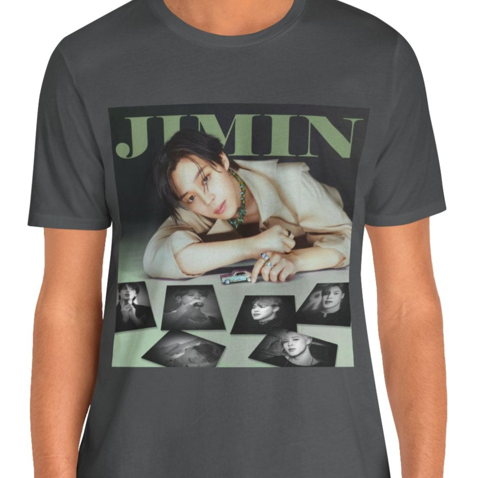 Jimin BTS Unisex T-Shirt in asphalt – A Playful Charm. A stylish design featuring Jimin leaning forward while interacting with a miniature car. Soft, muted tones and balanced lighting highlight his delicate features, complemented by black-and-white portrait prints that add an editorial touch. ModeK Vetements.