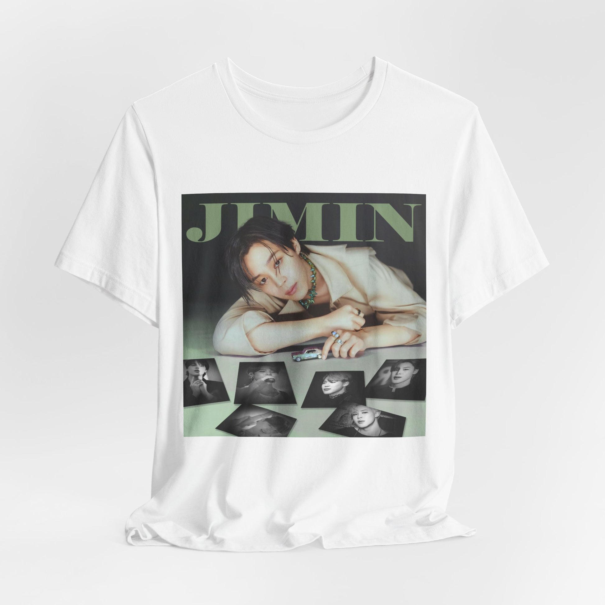 Draped Jimin BTS Unisex T-Shirt in white – A Playful Charm. A stylish design featuring Jimin leaning forward while interacting with a miniature car. Soft, muted tones and balanced lighting highlight his delicate features, complemented by black-and-white portrait prints that add an editorial touch. ModeK Vetements.