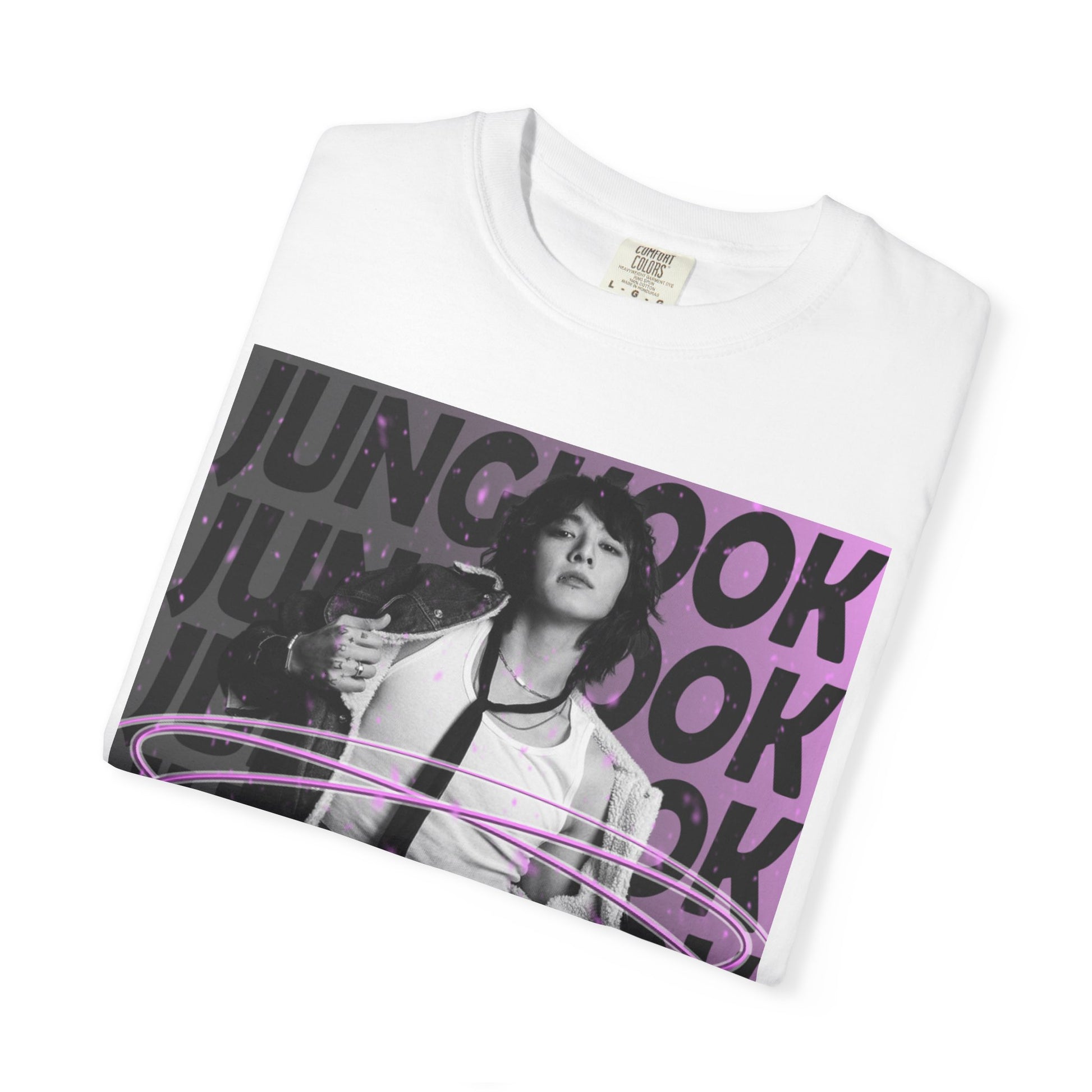 Folded unisex 100% ring-spun cotton T-Shirt in white, featuring BTS's Jungkook. He is posing against a dark background with "JUNGKOOK" repeated in large black typography and a charcoal-lavender gradient with pink paint splatters. Three glowing, thin magenta hoops encircle his waist, creating a sense of motion, making him even more provocative. From ModeK Vetements.