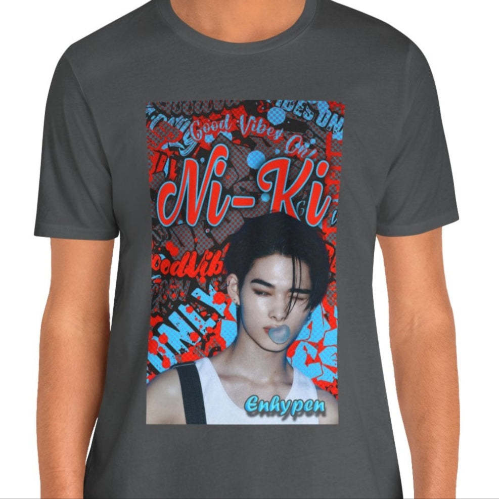 Unisex airlume cotton T-shirt in asphalt, featuring Ni-Ki of ENHYPEN layered into a bold graffiti-style design with Rosso Corsa red and Malibu Blue. The layout includes digital splashes, checkerboard effects, and a bubble gum moment frozen mid-pop. From ModeK Vetements.