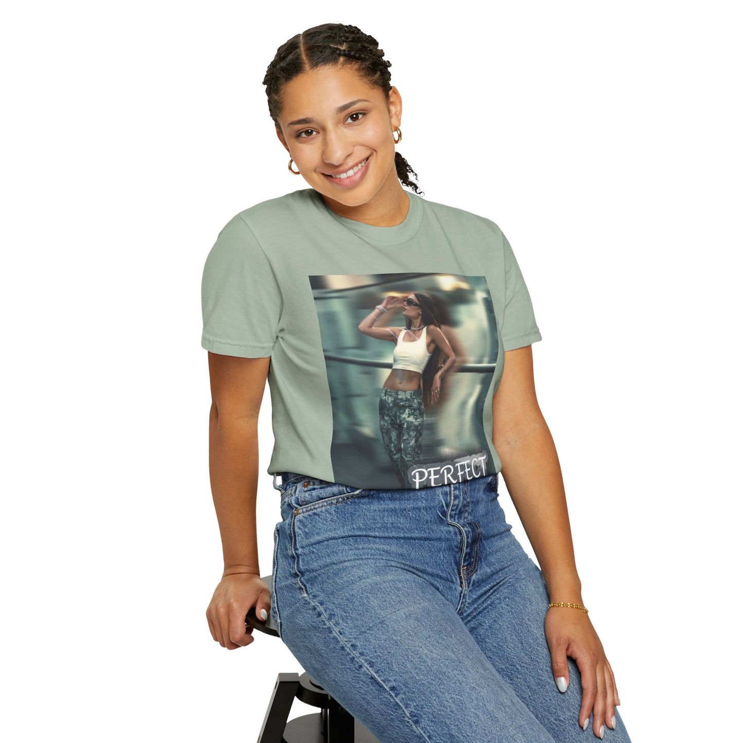 Sitting model wearing a unisex 100% ring-spun cotton t-shirt in bay, featuring a graphic design: a woman in tactical camo cargo pants and a white crop top stands as a sharp anchor against a blurry, cinematic urban background. The design also features a digital dispersion effect and electric blue rays, symbolizing the "Perfect Illusion" where brute force hides a deeper reality of tenderness and beauty. From ModeK Vetements.