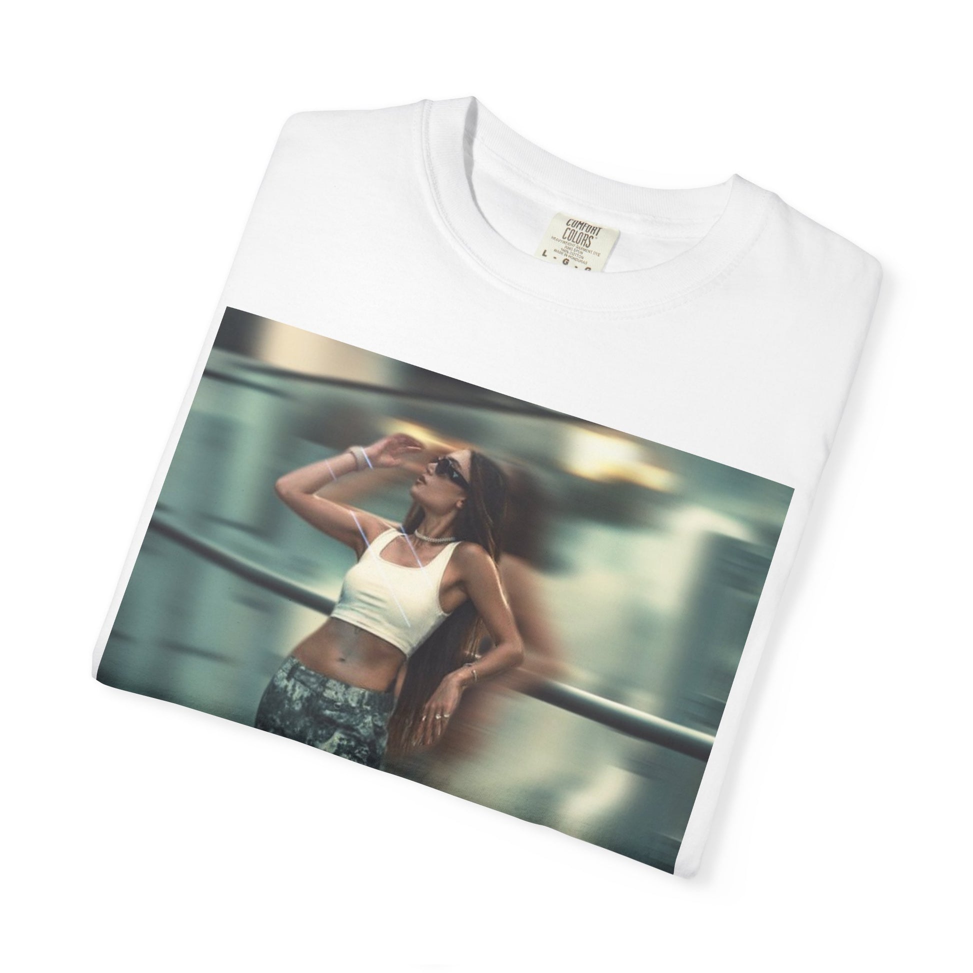 Folded unisex 100% ring-spun cotton t-shirt in white, featuring a graphic design: a woman in tactical camo cargo pants and a white crop top stands as a sharp anchor against a blurry, cinematic urban background. The design also features a digital dispersion effect and electric blue rays, symbolizing the "Perfect Illusion" where brute force hides a deeper reality of tenderness and beauty. From ModeK Vetements.