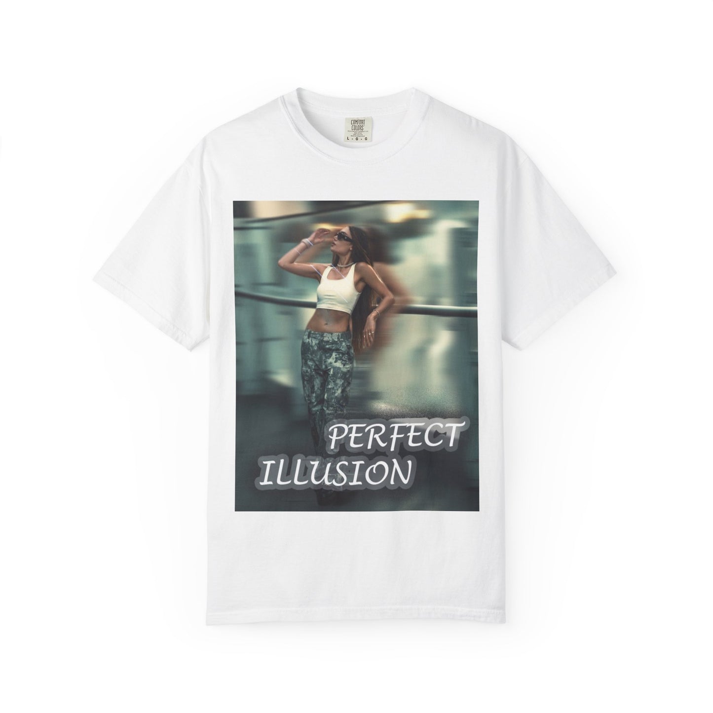 Hanging unisex 100% ring-spun cotton t-shirt in white, featuring a graphic design: a woman in tactical camo cargo pants and a white crop top stands as a sharp anchor against a blurry, cinematic urban background. The design also features a digital dispersion effect and electric blue rays, symbolizing the "Perfect Illusion" where brute force hides a deeper reality of tenderness and beauty. From ModeK Vetements.