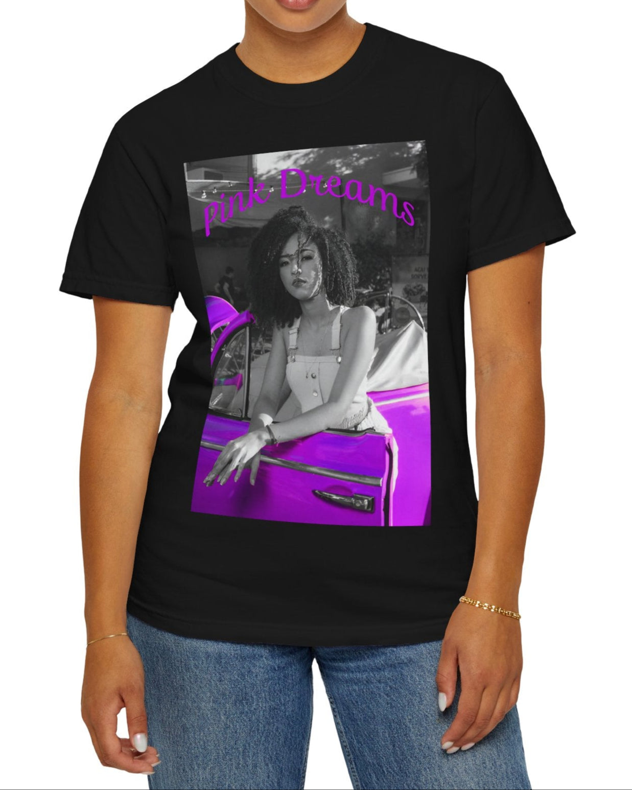 Unisex T-shirt in black, made from 100% ring-spun cotton featuring a printed design where a pinkish purple race car dominates a monochrome scene, with a girl leaning calmly against it. The words “Pink Dreams” curve above, evoking attitude, stillness, and the feeling of living on her own terms. From ModeK Vetements.