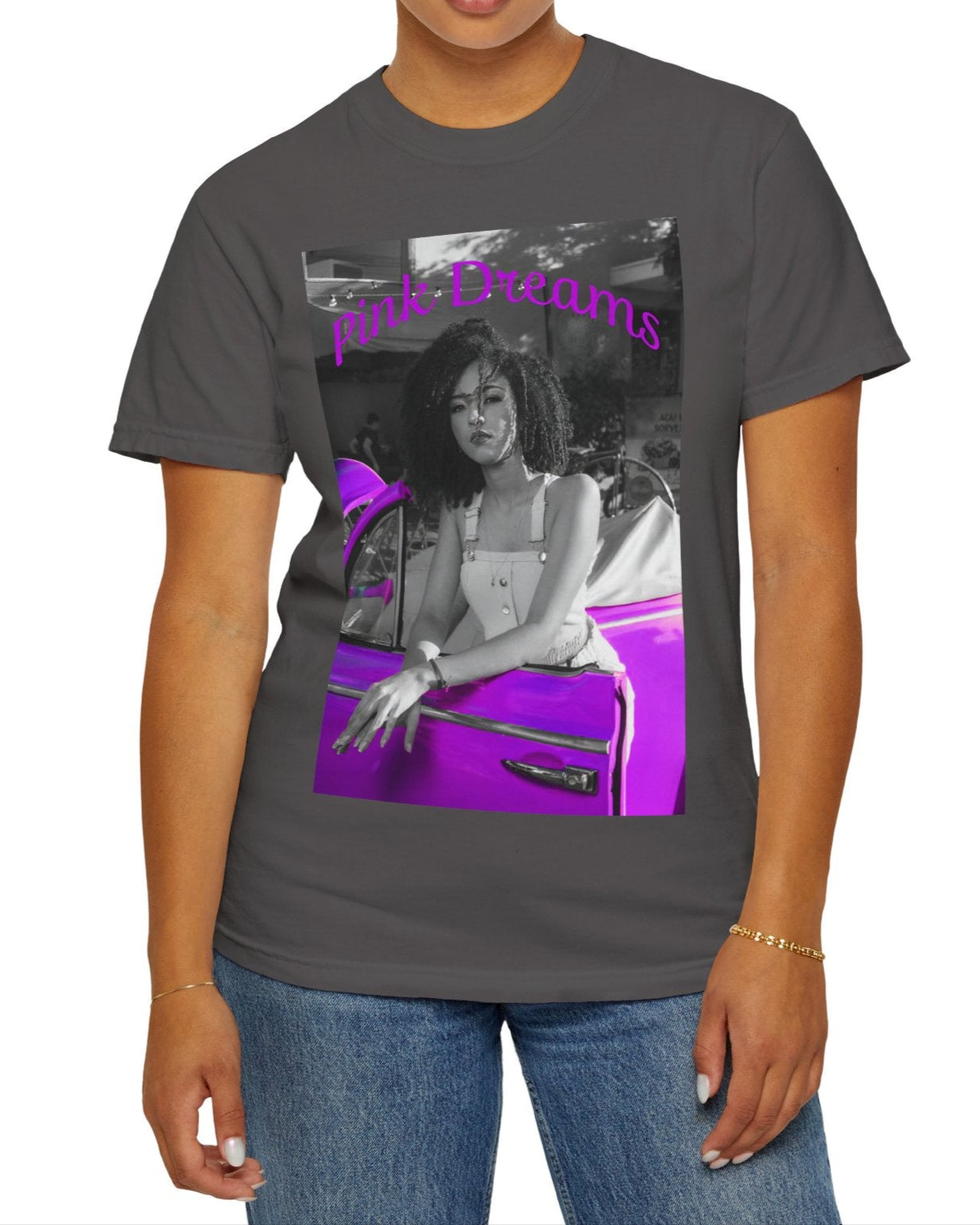 Unisex T-shirt in graphite, made from 100% ring-spun cotton featuring a printed design where a pinkish purple race car dominates a monochrome scene, with a girl leaning calmly against it. The words “Pink Dreams” curve above, evoking attitude, stillness, and the feeling of living on her own terms. From ModeK Vetements.