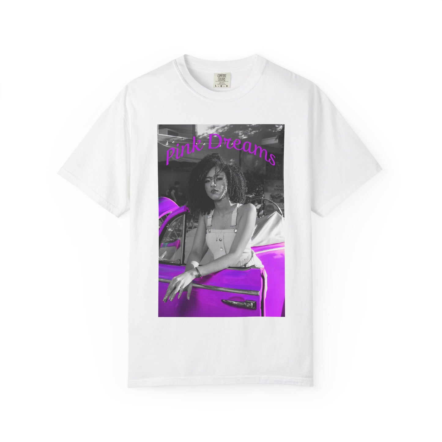 Flat Unisex T-shirt in white, made from 100% ring-spun cotton featuring a printed design where a pinkish purple race car dominates a monochrome scene, with a girl leaning calmly against it. The words “Pink Dreams” curve above, evoking attitude, stillness, and the feeling of living on her own terms. From ModeK Vetements.