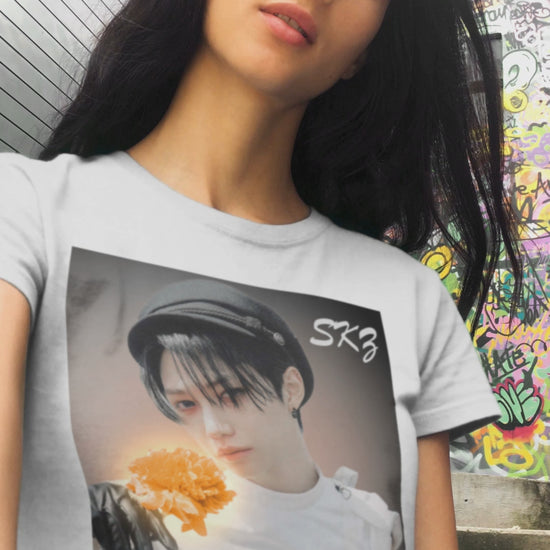 Video showcasing the Felix Stray Kids unisex T-shirt in white, inspired by the 143 MV. Features Felix in white costume with glowing orange flower, contrasted against a dark, cinematic background. ModeK Vetements.