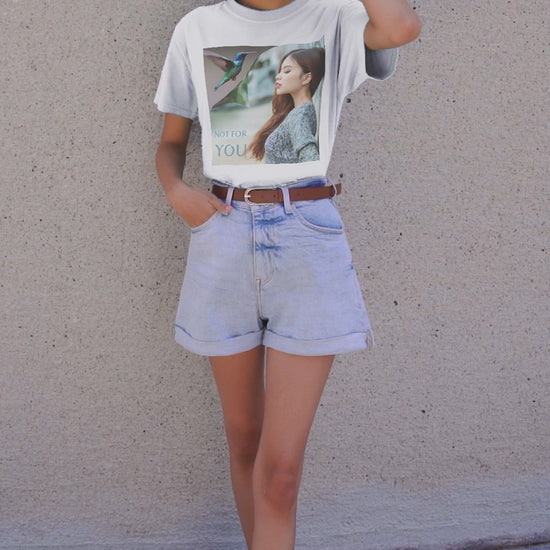 Video showcasing the Unisex airlume combed, ring-spun cotton T-shirt in white, featuring a turning-page effect that reveals a hummingbird in flight. Inspired by the lightness, color, and serenity of the bird, the design evokes grace, freedom, and a soul that seeks only the nectar of life. From ModeK Vetements.