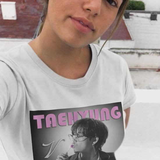 Video showcasing the V Taehyung BTS unisex t-shirt in white, featuring a black-and-white design with a pink lollipop and vintage pink lettering. Printed on 100% US cotton, ethically made and Oeko-Tex certified. ModeK Vetements.