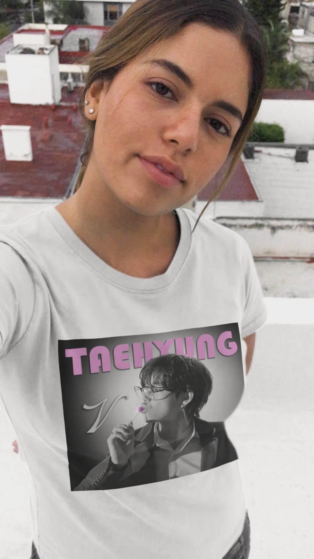 Video showcasing the V Taehyung BTS unisex t-shirt in white, featuring a black-and-white design with a pink lollipop and vintage pink lettering. Printed on 100% US cotton, ethically made and Oeko-Tex certified. ModeK Vetements.