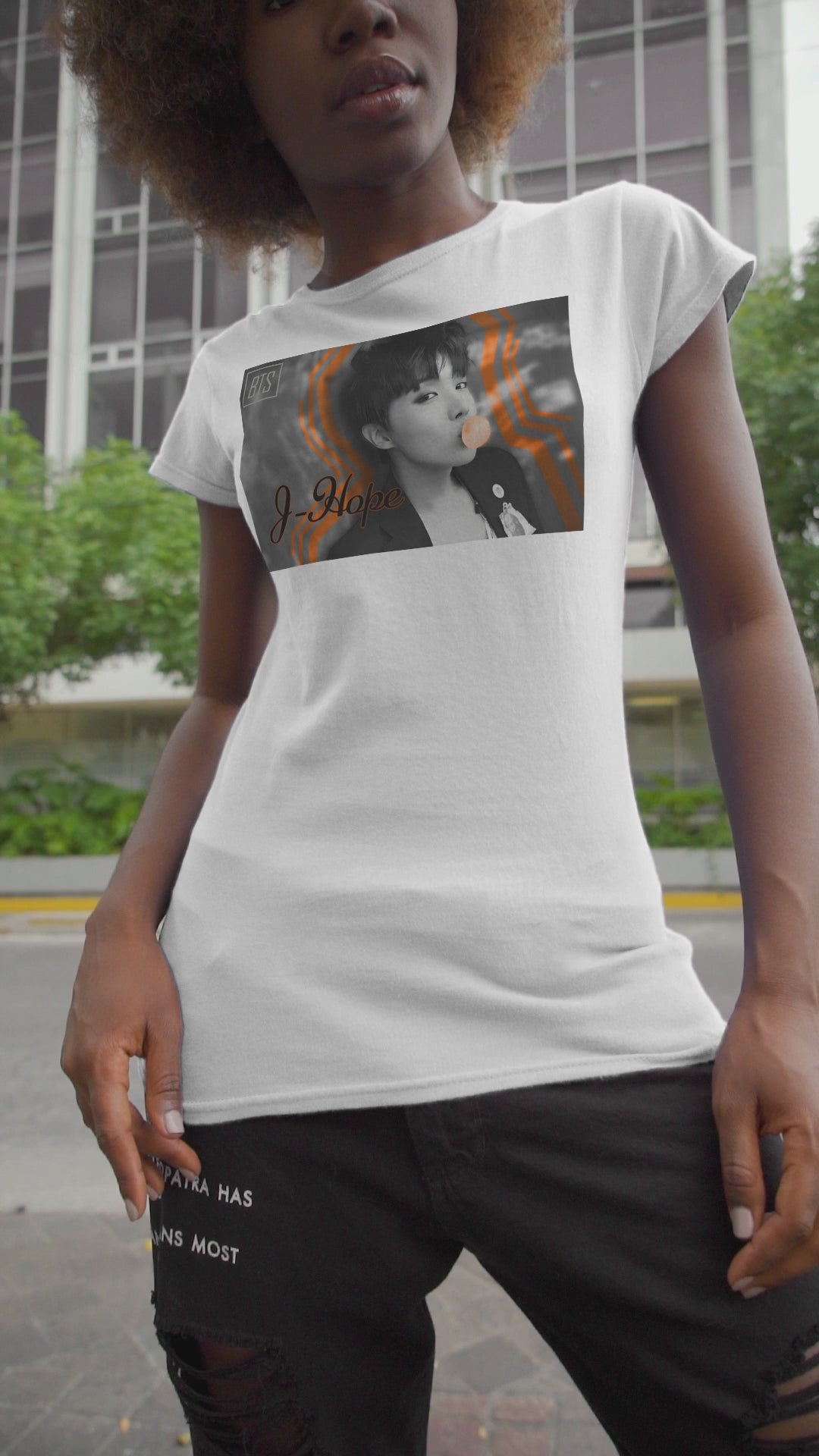 Video showcasing the Black-and-white portrait of J-Hope of BTS blowing peach bubblegum, accented with bold deep orange contour lines — playful and bold design on a unisex cotton T-shirt in white. ModeK Vetements.