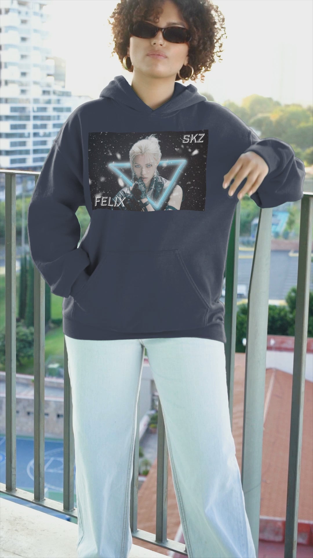 Video showcasing the Unisex cotton-poly blend hoodie in navy, featuring a visual print of Felix from Stray Kids, framed by a glowing blue neon triangle amid falling snow on a dark background. From ModeK Vetements.