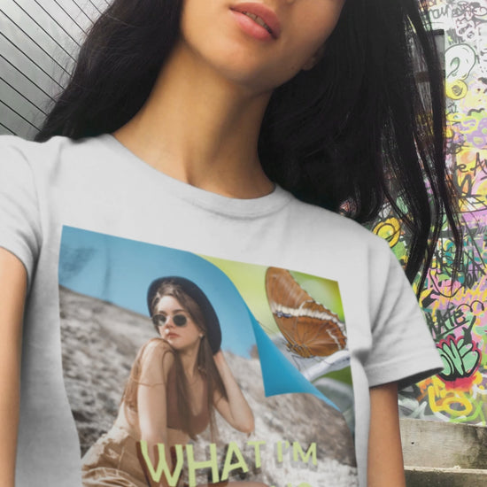 Video showcasing the unisex jersey T-Shirt in white featuring a woman sitting on a sunlit rocky beach with mint text “WHAT I’M FEELING.” A folded corner reveals a rusty-tipped page butterfly. — From ModeK Vetements.