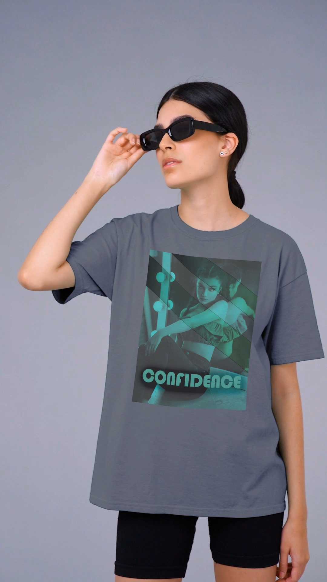 Video showcasing the Unisex heavy carded cotton T-shirt in faded indigo with a boxy fit, featuring a woman who sits in front of a softly lit vanity mirror, framed by diagonal tones of pine and sea green. Her expression is poised and calm, capturing quiet confidence without performance. From ModeK Vetements.