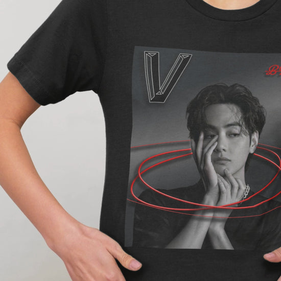 Video showcasing the unisex 100% cotton T-shirt in black. The front of the shirt displays a high-contrast black-and-white portrait of K-pop star V (Kim Taehyung) of BTS looking forward with a contemplative expression. Encircling him are vibrant red, glowing oval rings. A styled "V" appears in the top-left corner and a red "BTS" logo in the top-right corner. From ModeK Vetements.
