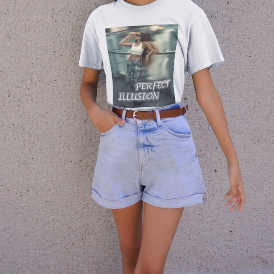 Video featuring a model wearing a unisex 100% ring-spun cotton t-shirt in white with a graphic design: a woman in tactical camo cargo pants and a white crop top stands as a sharp anchor against a blurry, cinematic urban background. The design also features a digital dispersion effect and electric blue rays, symbolizing the "Perfect Illusion" where brute force hides a deeper reality of tenderness and beauty. From ModeK Vetements.