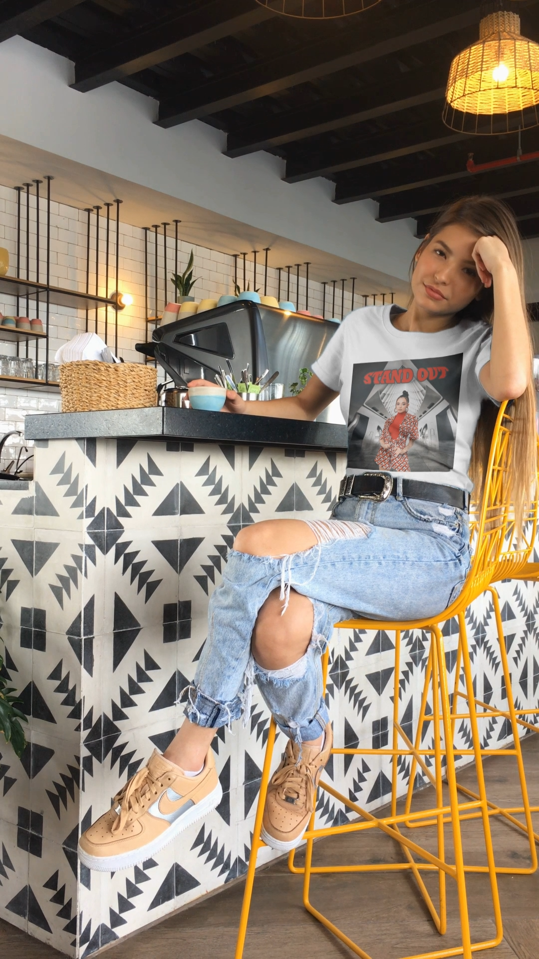 Video showcasing the Unisex airlume cotton T-Shirt in white, featuring a Woman in bold red geometric outfit standing confidently in a futuristic black-and-white architectural space. The "STAND OUT" in striking retro-style block font above her is a visual statement of individuality. From ModeK Vetements.