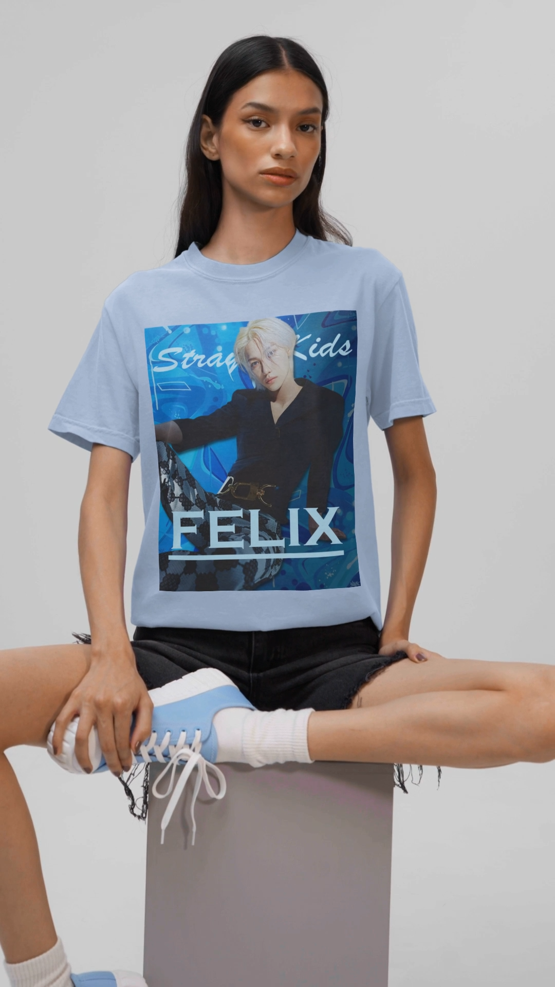 Video showcasing the unisex, 100% airlume combed & ring-spun cotton t-shirt in baby blue, featuring a graphic design. It shows Felix from Stray Kids in a provocative pose, wearing a structured black suit jacket and oriental-style patterned pants. The background is a multi-toned blue graffiti. From ModeK Vetements.