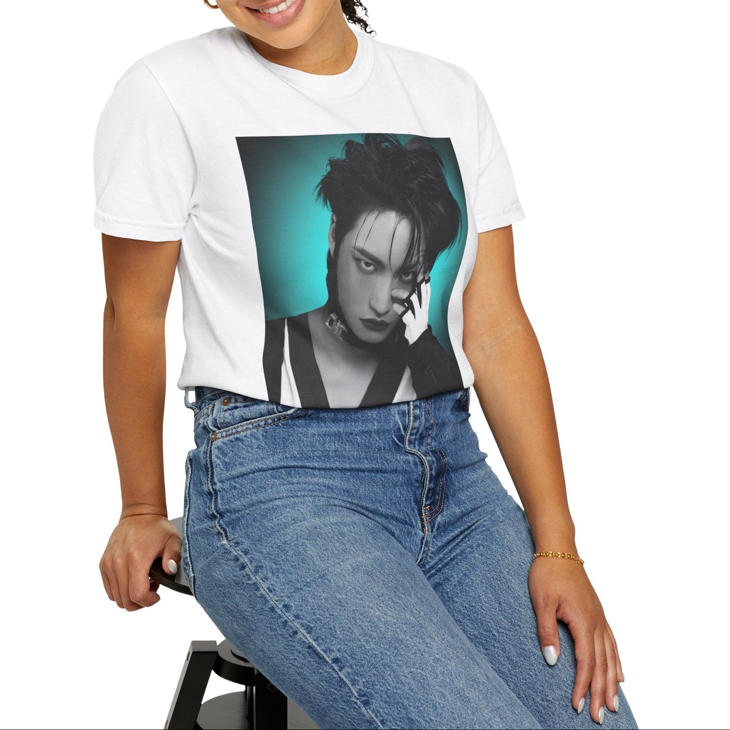 Model sitting on a chair and showcasing the Seonghwa ATEEZ Unisex T-Shirt in white – Experiment in Contrasts. A striking black-and-white portrait of Seonghwa with dramatic lighting, deep shadows, and a piercing gaze. His darkened lips add an intense edge, while a bold teal glow surrounds him, creating a contrast between elegance and raw energy. ModeK Vetements.