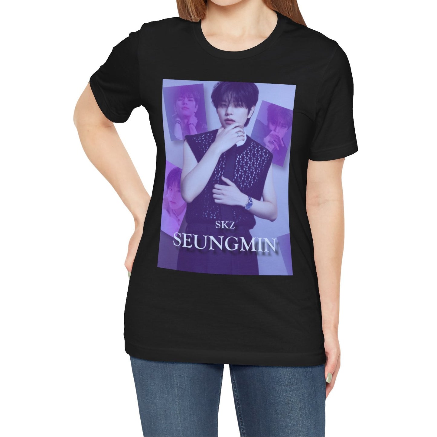 Female model showcasing the unisex, jersey, airlume combed and ringspun cotton T-Shirt in black, with a graphic design. It features Stray Kids' Seungmin in a sleeveless crochet top and blueberry tie. He poses thoughtfully against a periwinkle backdrop with a mist-covered collage of lavender, magazine-style photos. At the bottom, "SKZ SEUNGMIN" is written in pale lily-blue with a soft drop shadow. From ModeK Vetments.