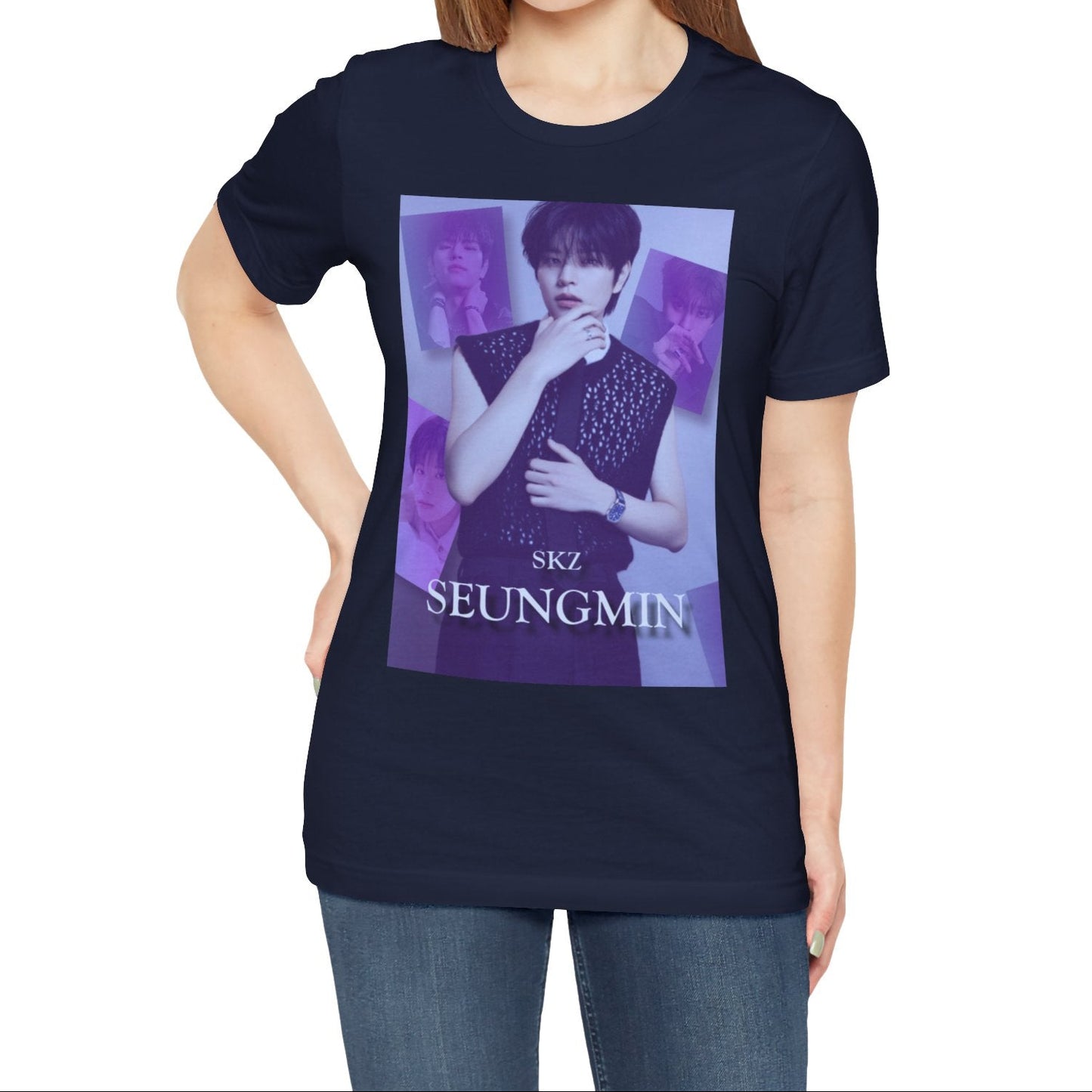 Female model showcasing the unisex, jersey, airlume combed and ringspun cotton T-Shirt in navy, with a graphic design. It features Stray Kids' Seungmin in a sleeveless crochet top and blueberry tie. He poses thoughtfully against a periwinkle backdrop with a mist-covered collage of lavender, magazine-style photos. At the bottom, "SKZ SEUNGMIN" is written in pale lily-blue with a soft drop shadow. From ModeK Vetments.