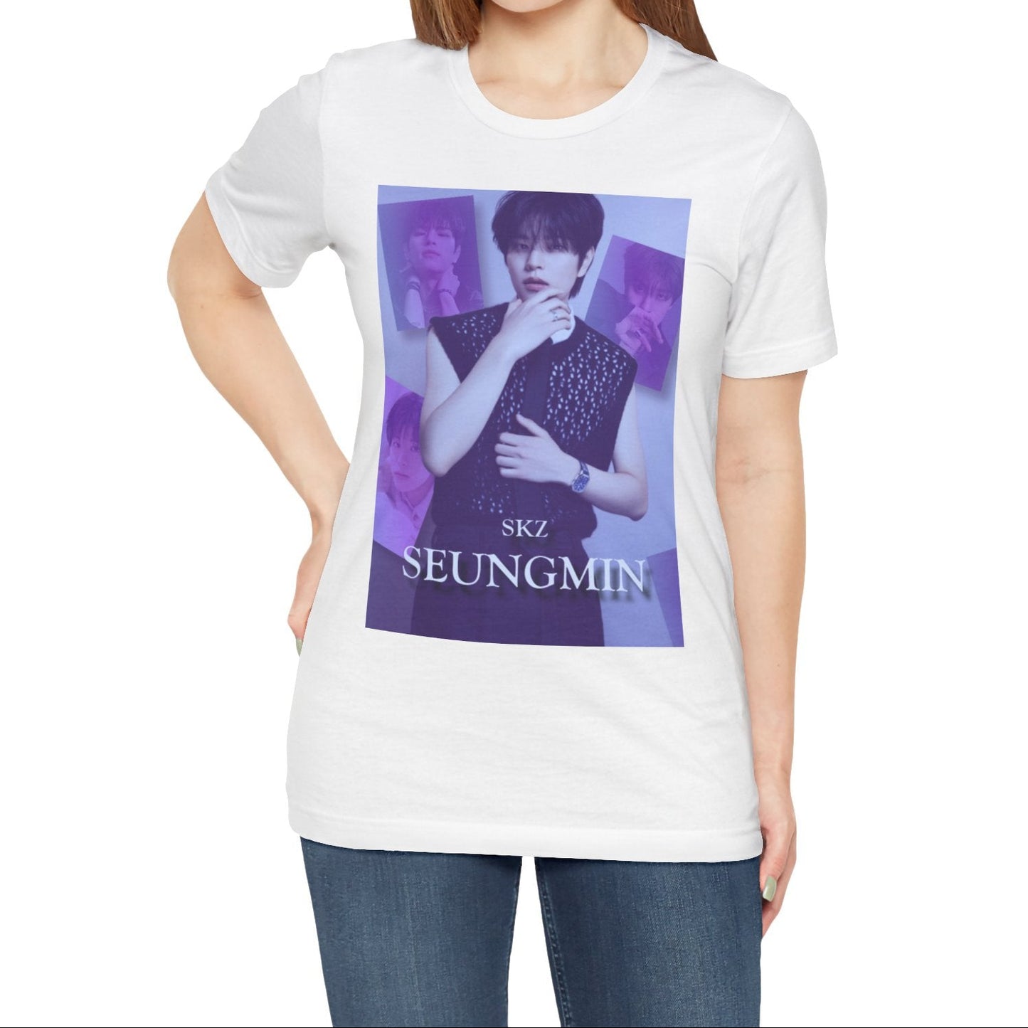 Female model showcasing the unisex, jersey, airlume combed and ringspun cotton T-Shirt in white, with a graphic design. It features Stray Kids' Seungmin in a sleeveless crochet top and blueberry tie. He poses thoughtfully against a periwinkle backdrop with a mist-covered collage of lavender, magazine-style photos. At the bottom, "SKZ SEUNGMIN" is written in pale lily-blue with a soft drop shadow. From ModeK Vetments.
