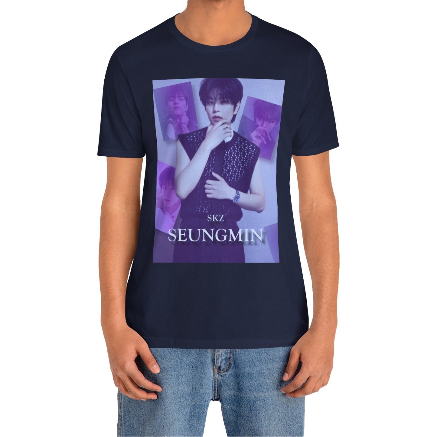Male model showcasing the unisex, jersey, airlume combed and ringspun cotton T-Shirt in navy, with a graphic design. It features Stray Kids' Seungmin in a sleeveless crochet top and blueberry tie. He poses thoughtfully against a periwinkle backdrop with a mist-covered collage of lavender, magazine-style photos. At the bottom, "SKZ SEUNGMIN" is written in pale lily-blue with a soft drop shadow. From ModeK Vetments.