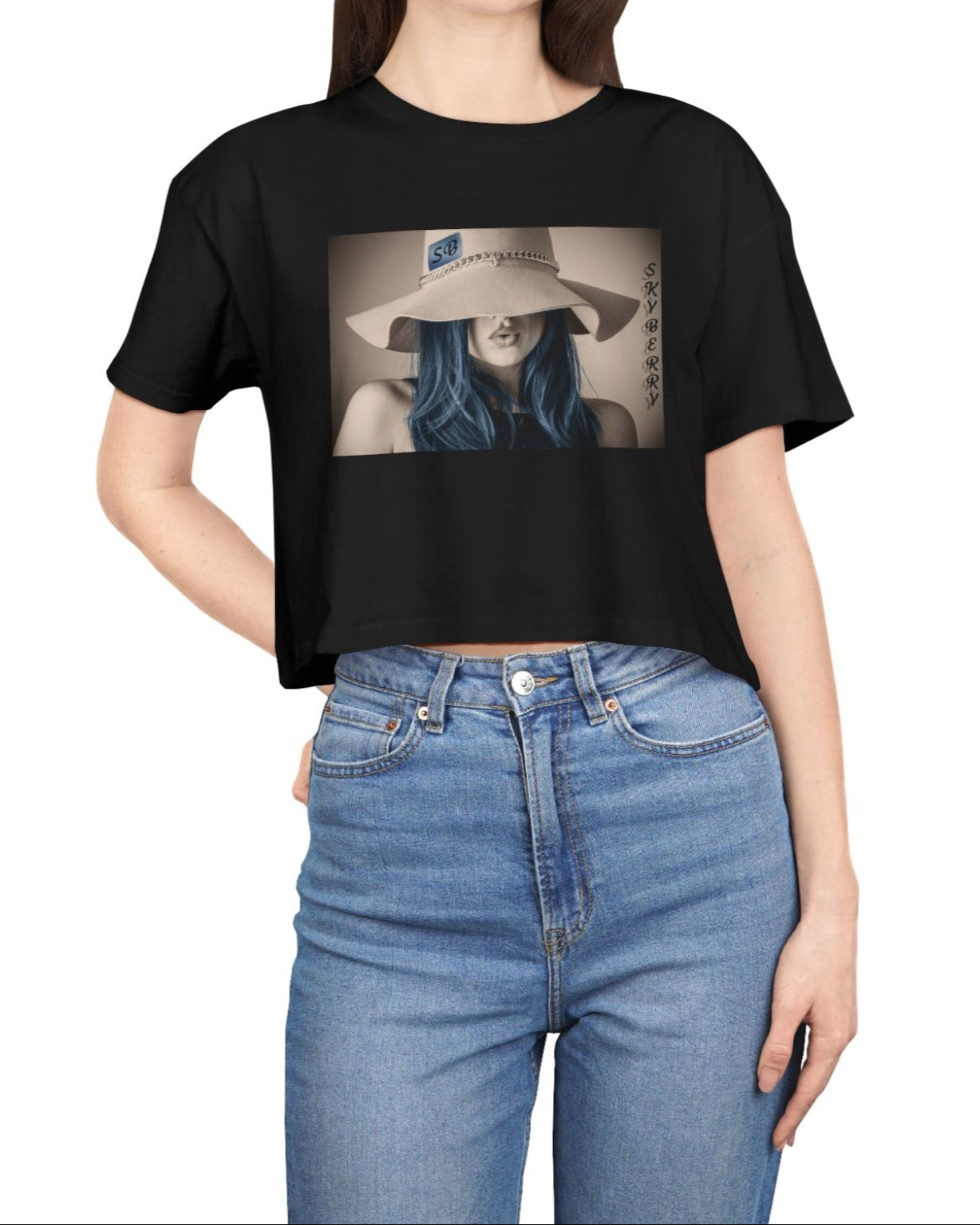 Design printed on a women’s crop tee in black, made from 100% combed cotton. It features a stylized woman with soft blue hair and a wide felt hat, her gaze hidden. Above her, the word “Skyberry” appears in black lettering. The composition evokes quiet mystery and the feeling of a summer mirage. From Modek Vetements.