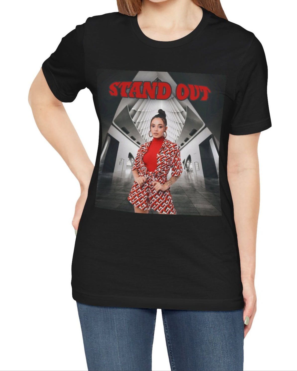 Unisex airlume cotton T-Shirt in black, featuring a Woman in bold red geometric outfit standing confidently in a futuristic black-and-white architectural space. The "STAND OUT" in striking retro-style block font above her is a visual statement of individuality. From ModeK Vetements.