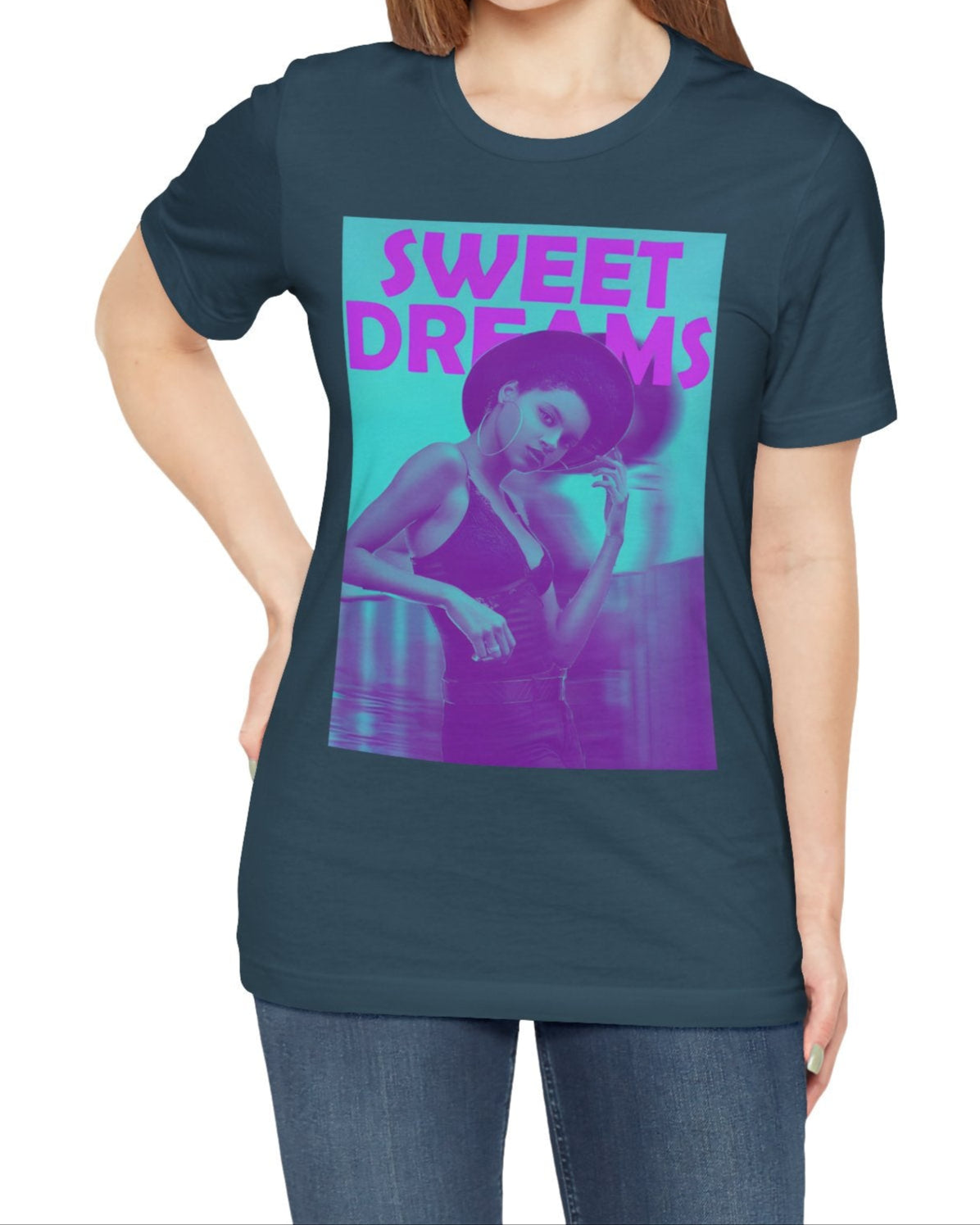 Unisex airlume cotton t-shirt in deep teal, featuring a woman in a wide-brimmed hat appearing clearly over a blurred motion version of herself, as if caught between dream and sleep. The lilac-pink words “SWEET DREAMS” float above on a medium turquoise background, evoking the gentle melancholy of May evenings. From ModeK Vetements.