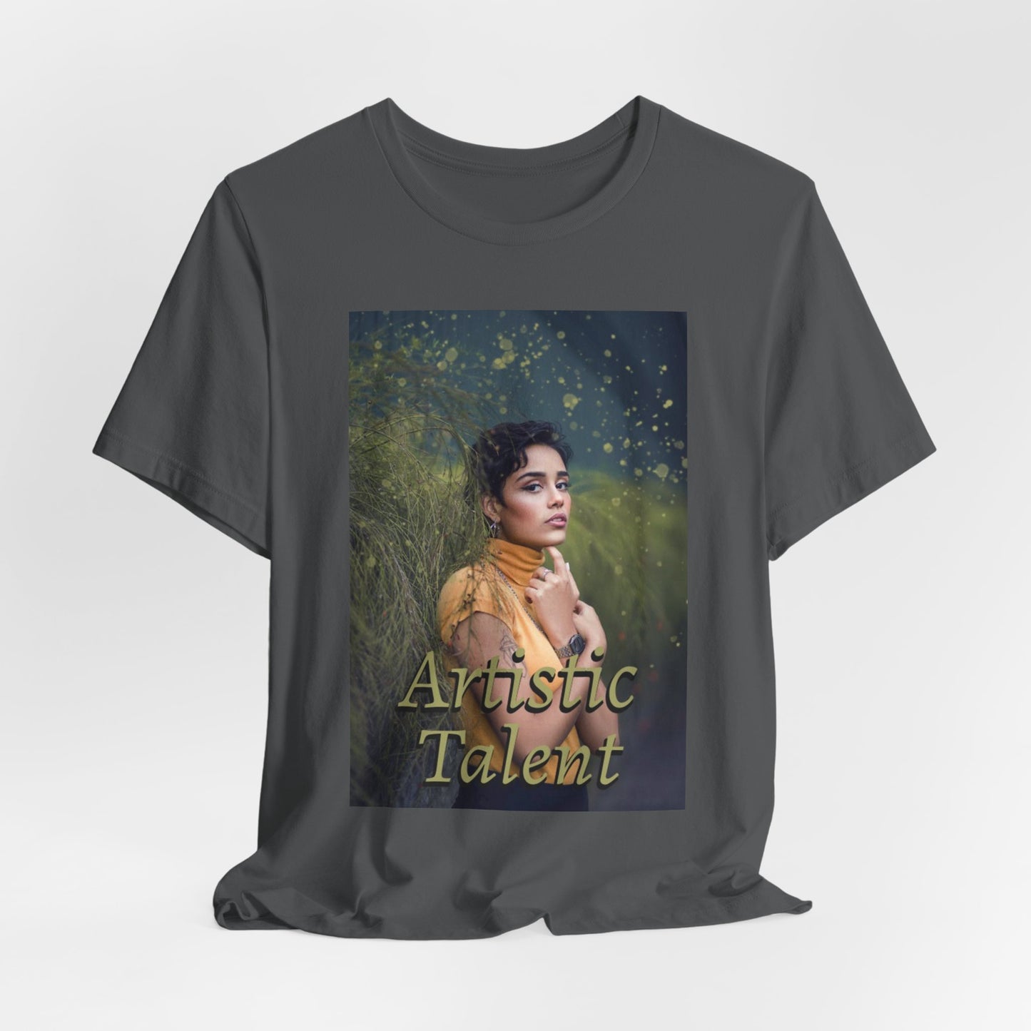 Draping unisex 100% airlume combed and ring-spun cotton t-shirt in asphalt featuring a woman in a yellow turtleneck. The image is layered with golden paint splashes creating a sense of motion and "Artistic Talent" where the subject looks real enough to step out of the picture. From ModeK Vetements.